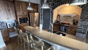A modern kitchen with a central island, wooden bar stools, stainless steel appliances, and a stone accent wall. - Luxury Mountain Retreat Near Midway & Park City – Sleeps 10 (Heber City)