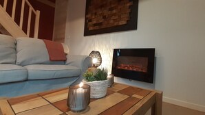 Una sala de estar con sofá, una mesa de centro con vela, chimenea y televisor montado en la pared.