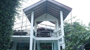 A two-story building with a covered balcony and a glass enclosure at the ground level.