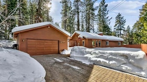 Une cabane avec un garage et une véranda couverte, entourée de neige et de grands pins.