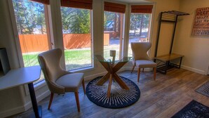 Une pièce baignée de lumière naturelle, avec une table en verre entourée de chaises, de grandes fenêtres équipées de stores et un plancher en bois.