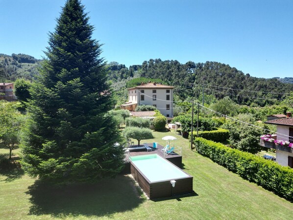 Zona residencial con un gran árbol de hoja perenne, una piscina y un edificio con tejado de tejas.