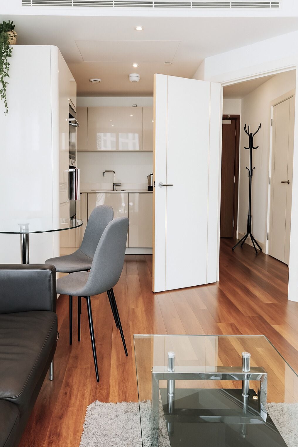 Ein modernes Wohnzimmer mit einem Glastisch, grauen Sesseln, einem schwarzen Sofa und einem Kleiderständer.