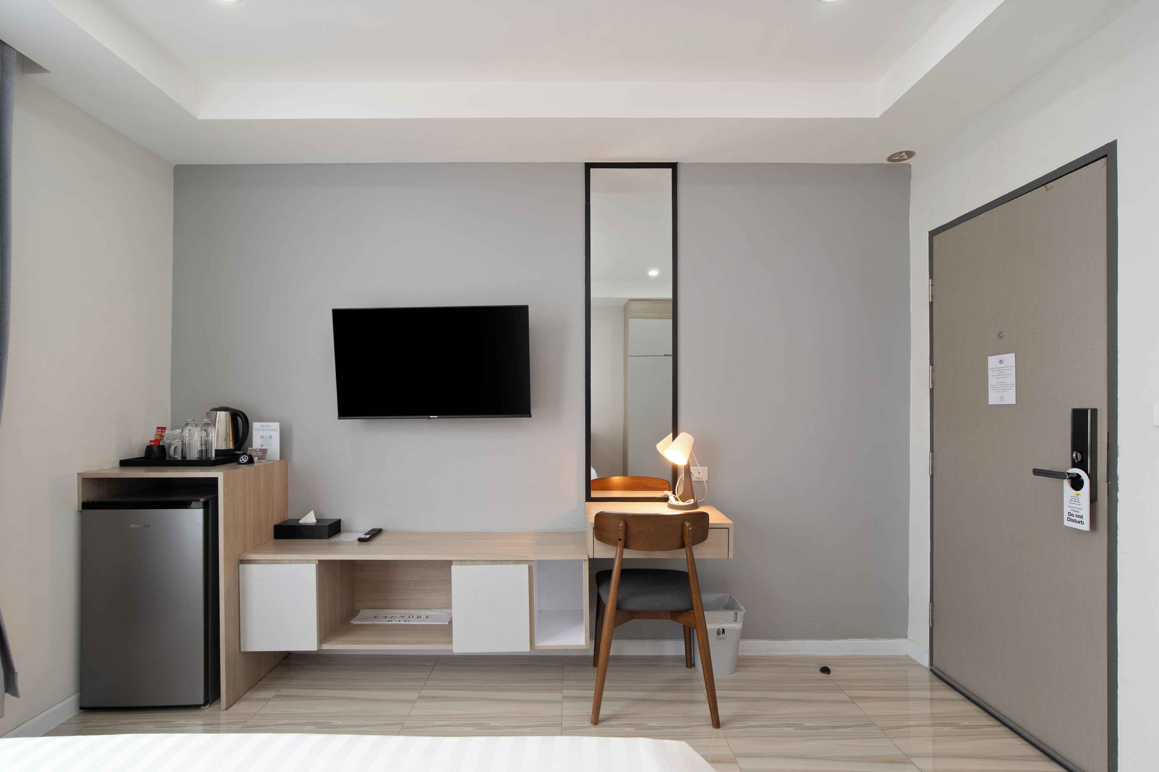 A modern hotel room with a bed, a desk with a chair, a television, and a refrigerator.