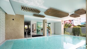 A modern indoor swimming pool with clear blue water, a glass floor, and a view of the outside. - The Riski Hotel at Bangphlat Station (Bangkok)