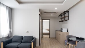 A modern hotel room with a grey sofa, a small round table, a wooden cabinet, and a bed in the background. - The Riski Hotel at Bangphlat Station (Bangkok)