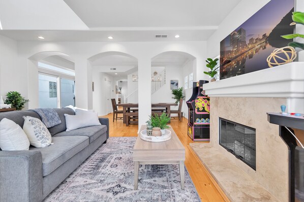 A modern living room with a grey sofa, a coffee table, and a fireplace. There is a staircase leading to an upper floor.