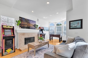 A living room with a fireplace, a gaming console, a sofa, and a large window.