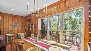 A wooden dining room with a large table set for four, a chandelier, and a view of the outdoors through large windows.
