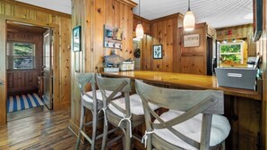 A rustic kitchen with wooden walls, a bar area with stools, and a hanging light fixture.