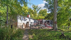 A rustic cabin with a stone chimney, a wooden deck, and a staircase leading to the entrance.
