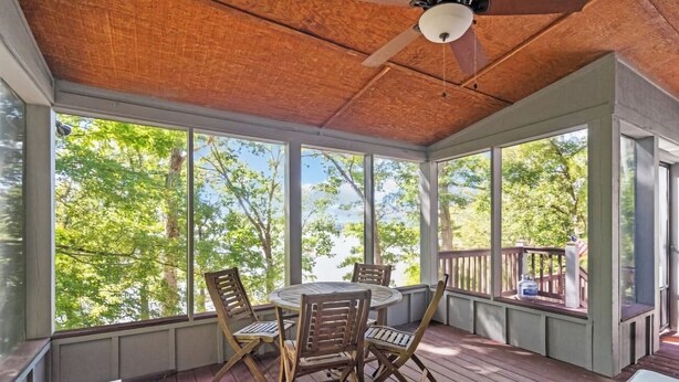 A covered outdoor seating area with a round table and chairs, large windows, and a ceiling fan.