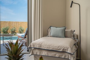 A bedroom with a bed, a bedside lamp, and a view of a pool and outdoor furniture.