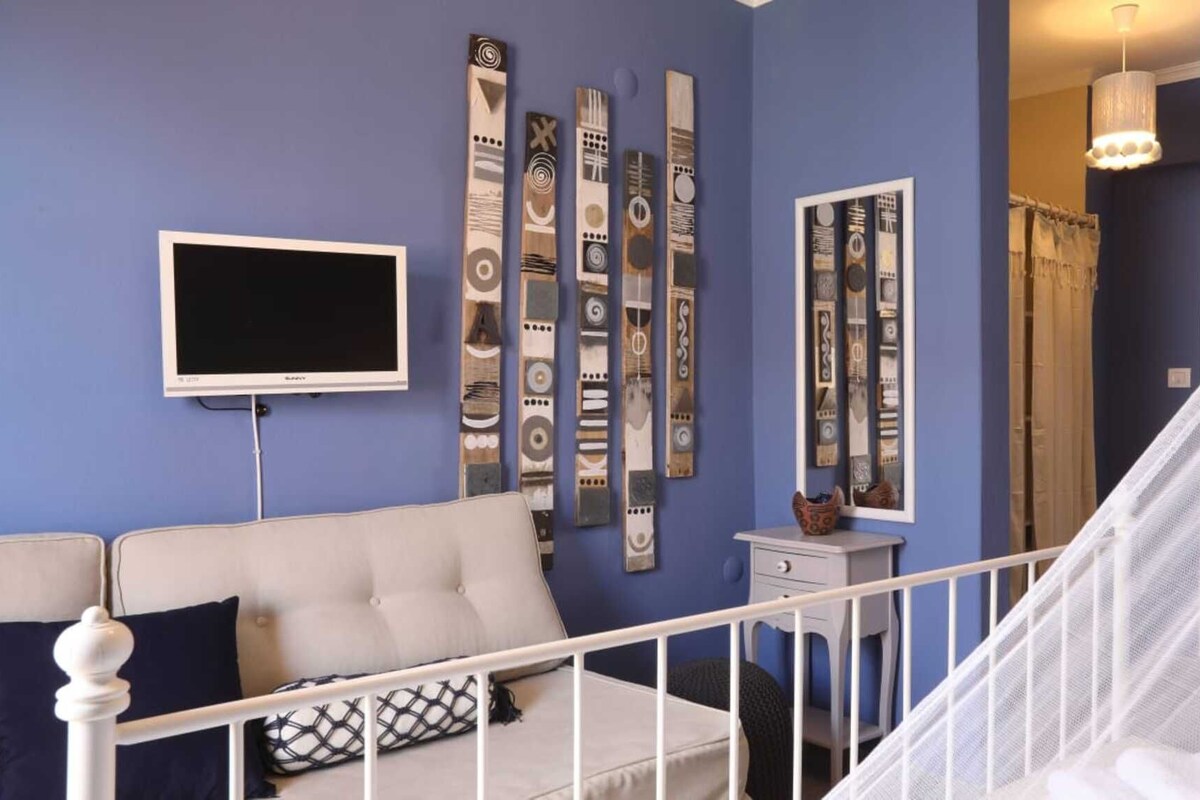 A room with a white sofa, a flat-screen TV, and a staircase with a white railing.