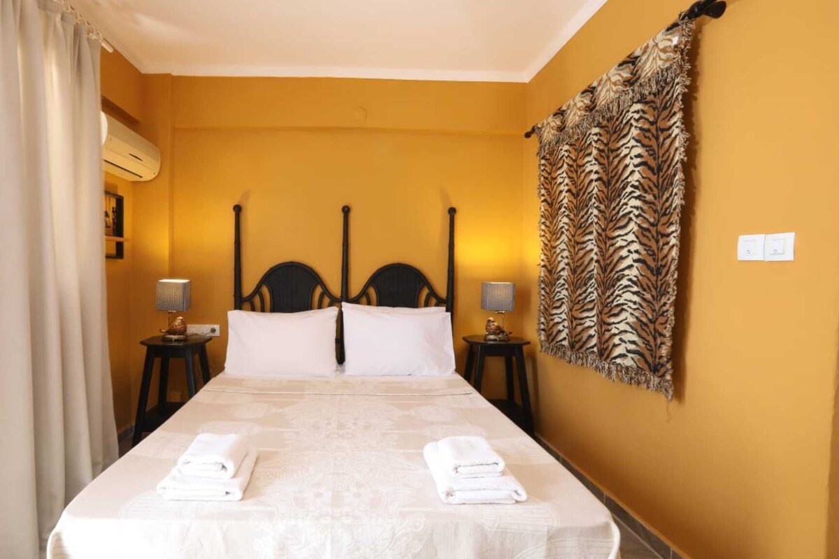 A hotel room with a bed, two bedside tables, a wall-mounted air conditioner, a zebra-patterned tapestry, and a curtain.