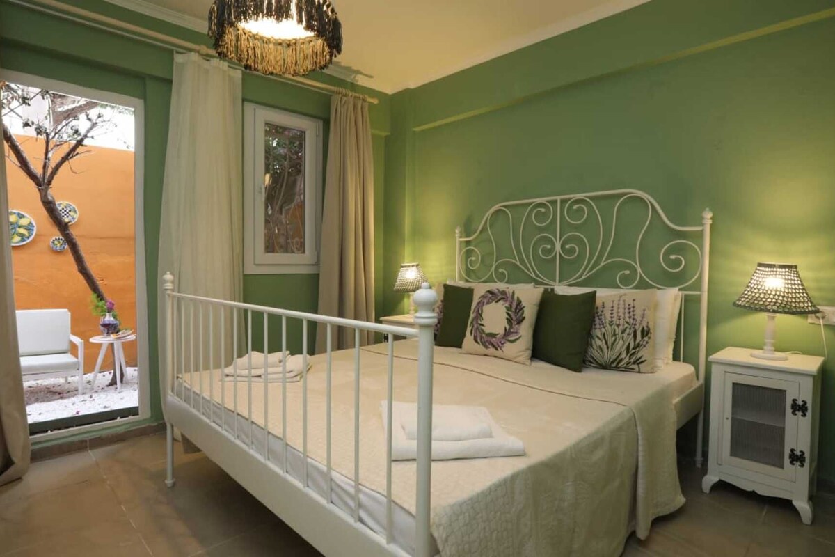 A bedroom with a bed, two bedside tables with lamps, a window with curtains, and a view of an outdoor area with a chair and a table.