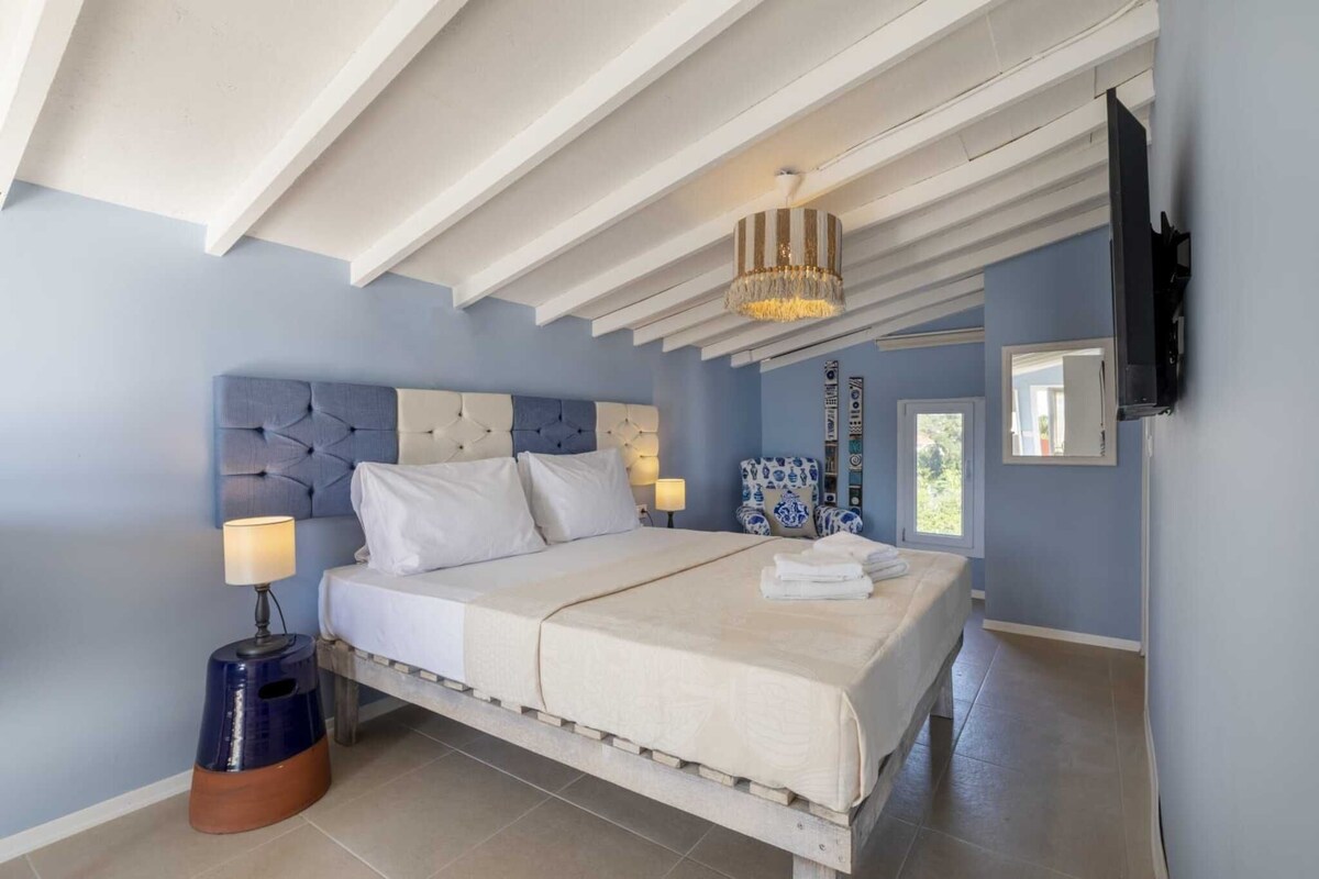 A bedroom with a bed, bedside lamps, a TV, and a decorative chair.