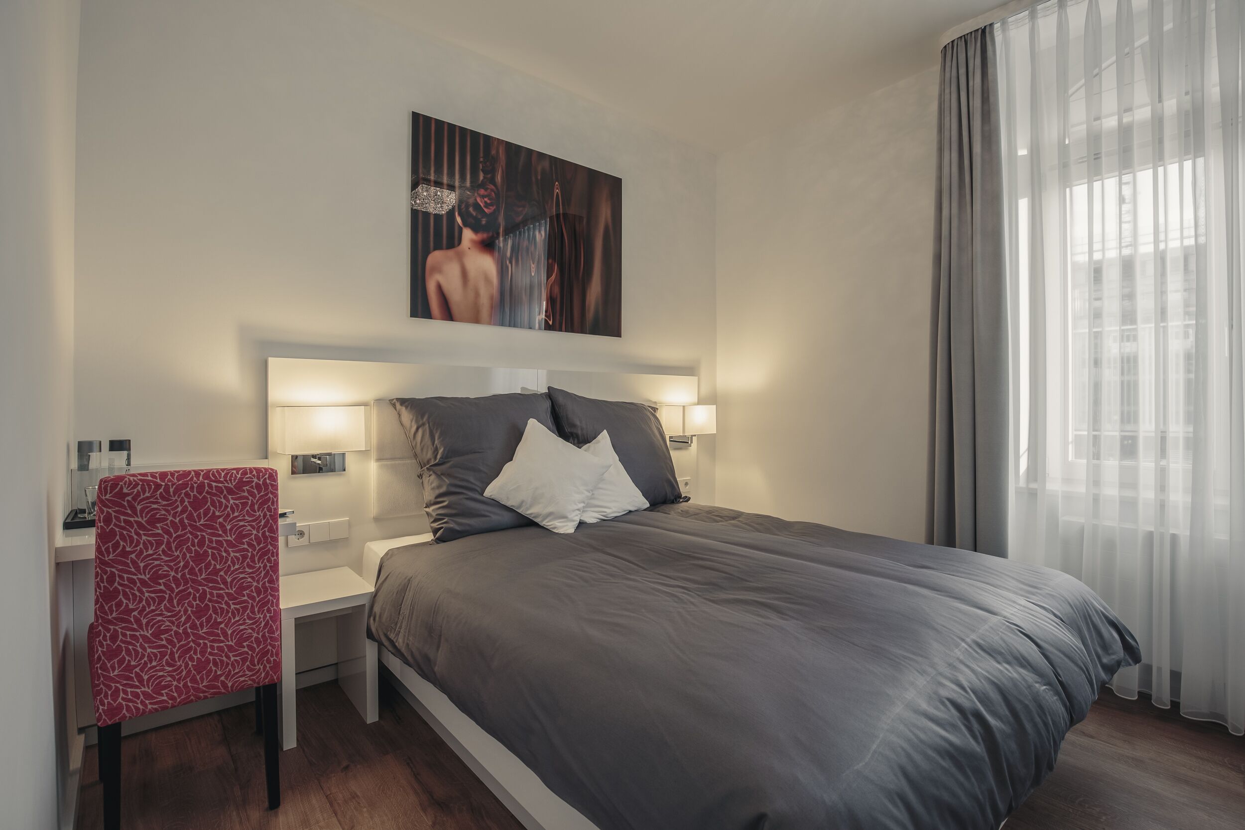 Una habitación de hotel moderna con una cama grande, lámparas de noche, un escritorio y una silla.
