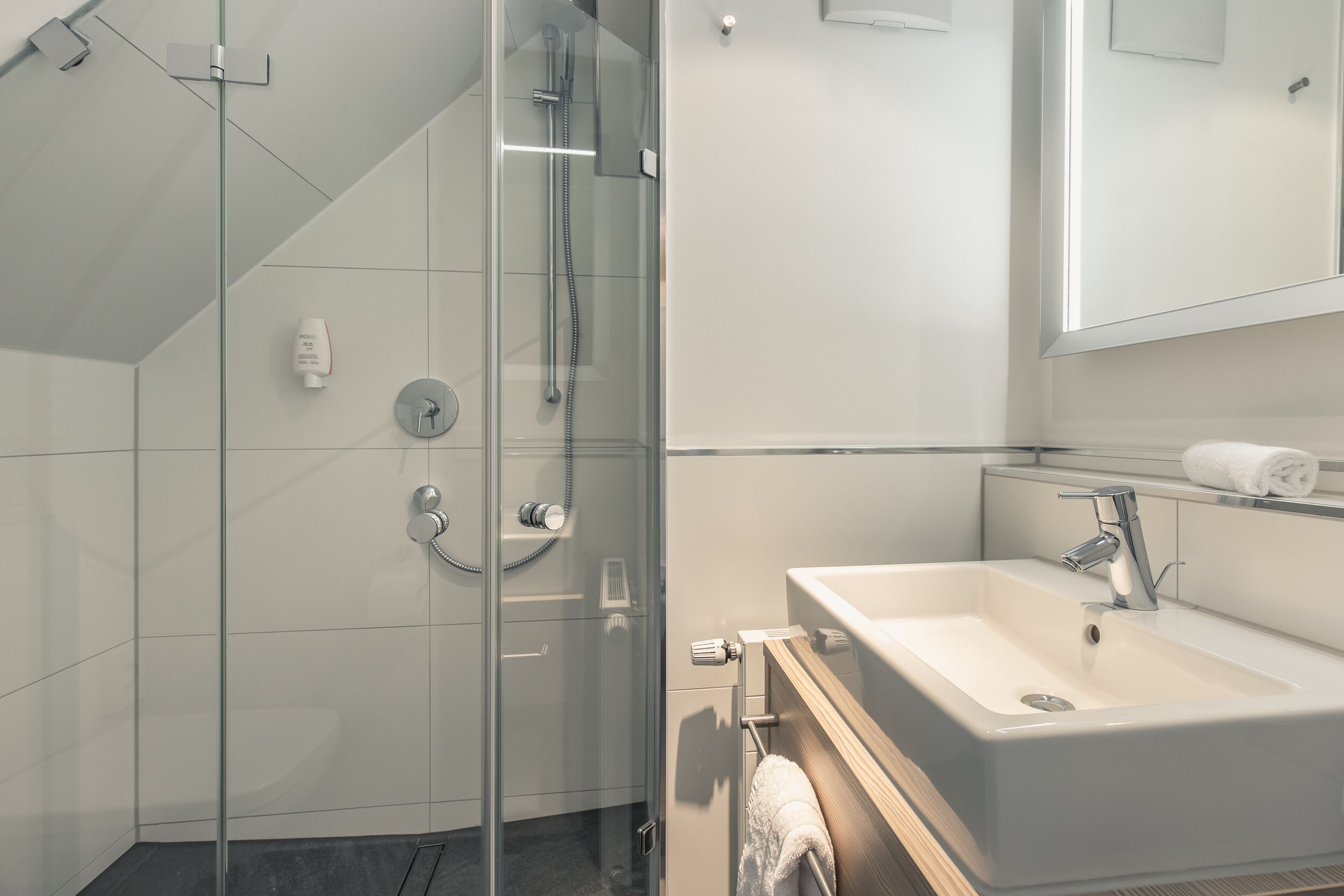 Un baño moderno con ducha de vidrio, lavamanos y espejo.