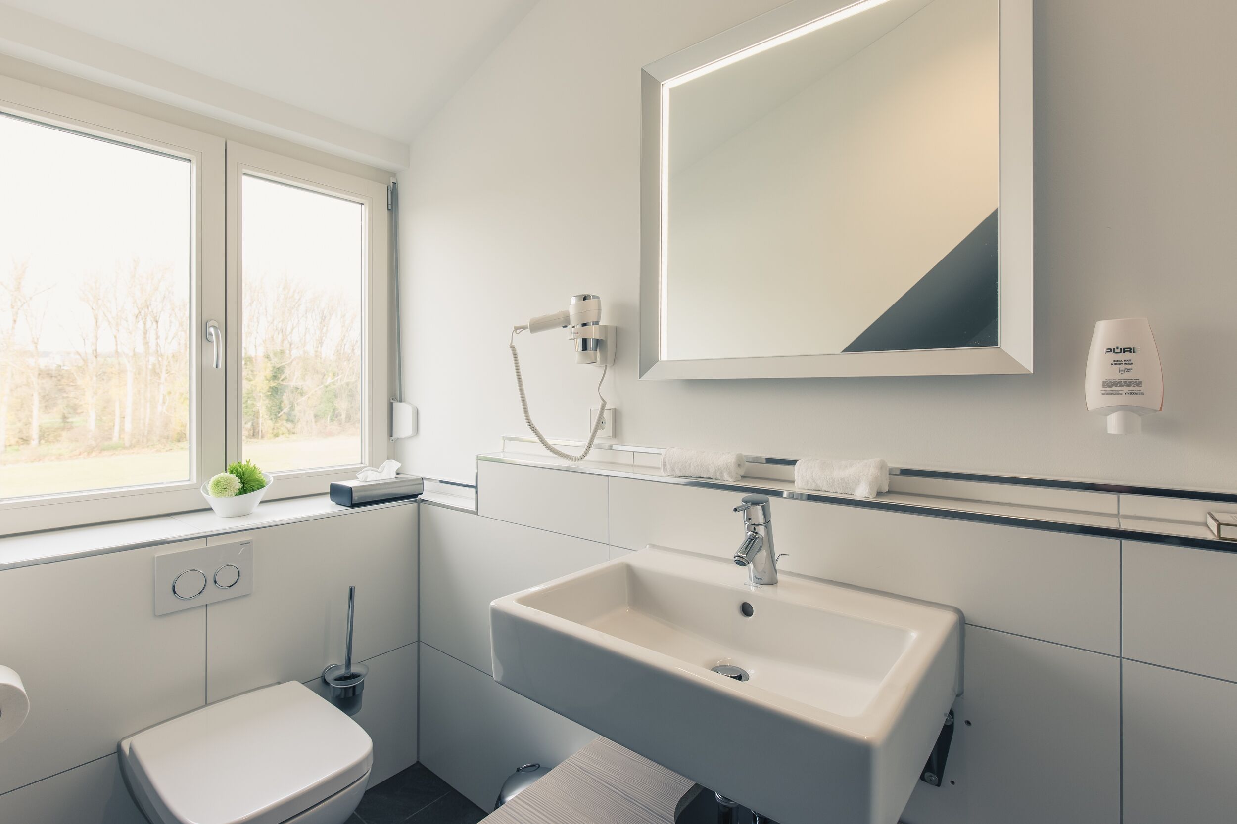 A modern bathroom with a white sink, a large mirror, and a window.