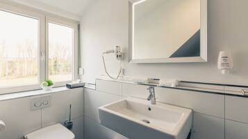 A modern bathroom with a white sink, a large mirror, and a window.