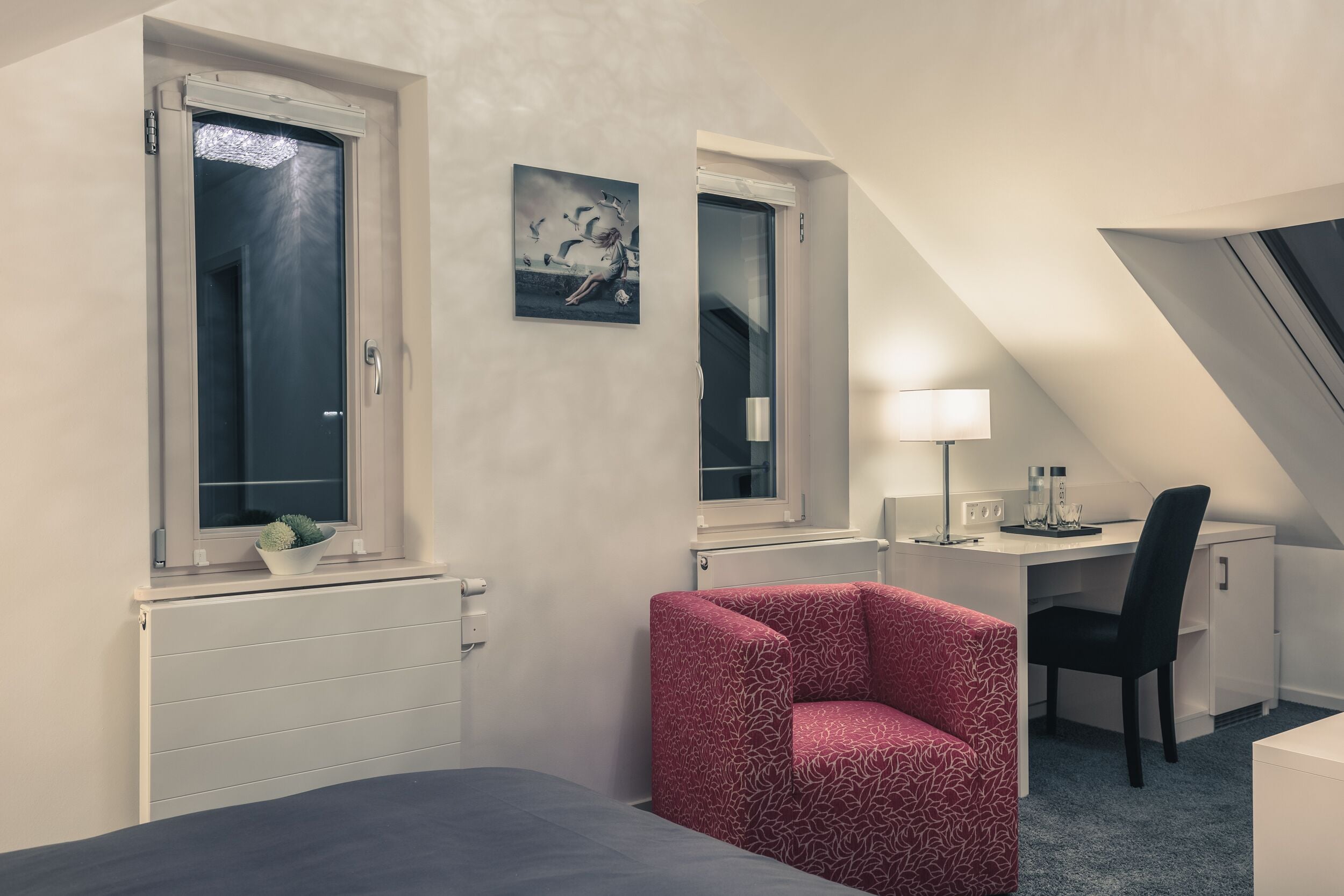 A bedroom with a bed, a desk, a chair, a radiator, and a window.