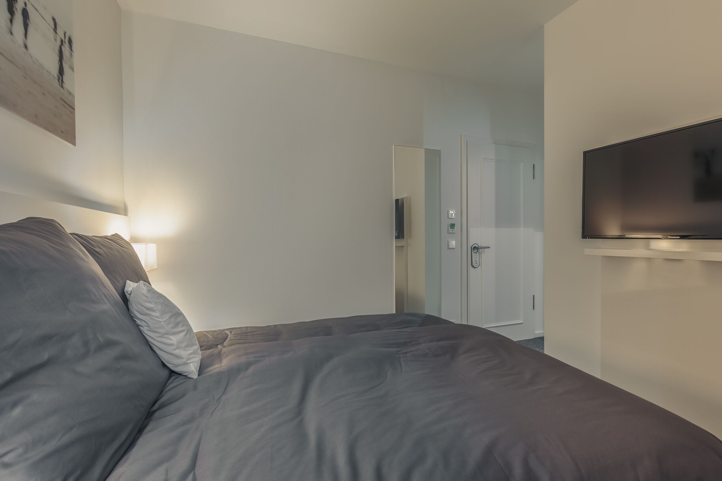 A modern bedroom with a bed, a TV, and a door leading to a bathroom.