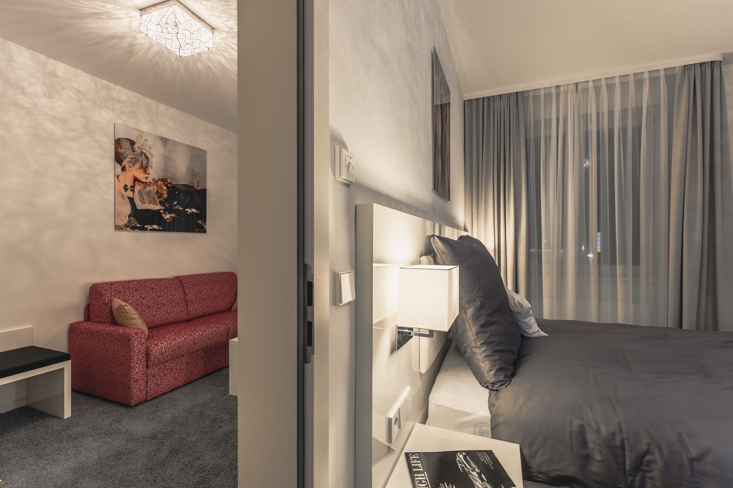 Una habitación de hotel con un sofá rojo, una cama con ropa de cama gris, una mesita de noche y un tocador.