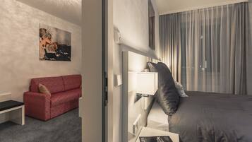 Una habitación de hotel con un sofá rojo, una cama con ropa de cama gris, una mesita de noche y un tocador.