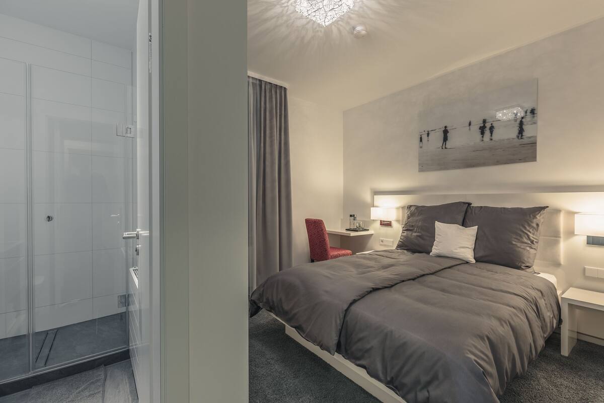 Una habitación de hotel moderna con una cama grande, una silla roja, una mesita de noche y una lámpara en el techo.