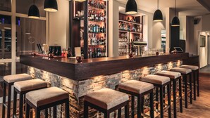 Un espace bar doté d’un comptoir en pierre, de plusieurs tabourets de bar et d’un éclairage suspendu.