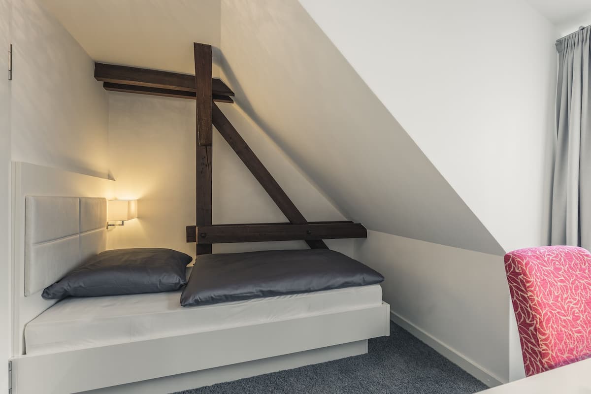 Una cama estilo loft pequeña y blanca, con cabecera de madera y dos almohadas.