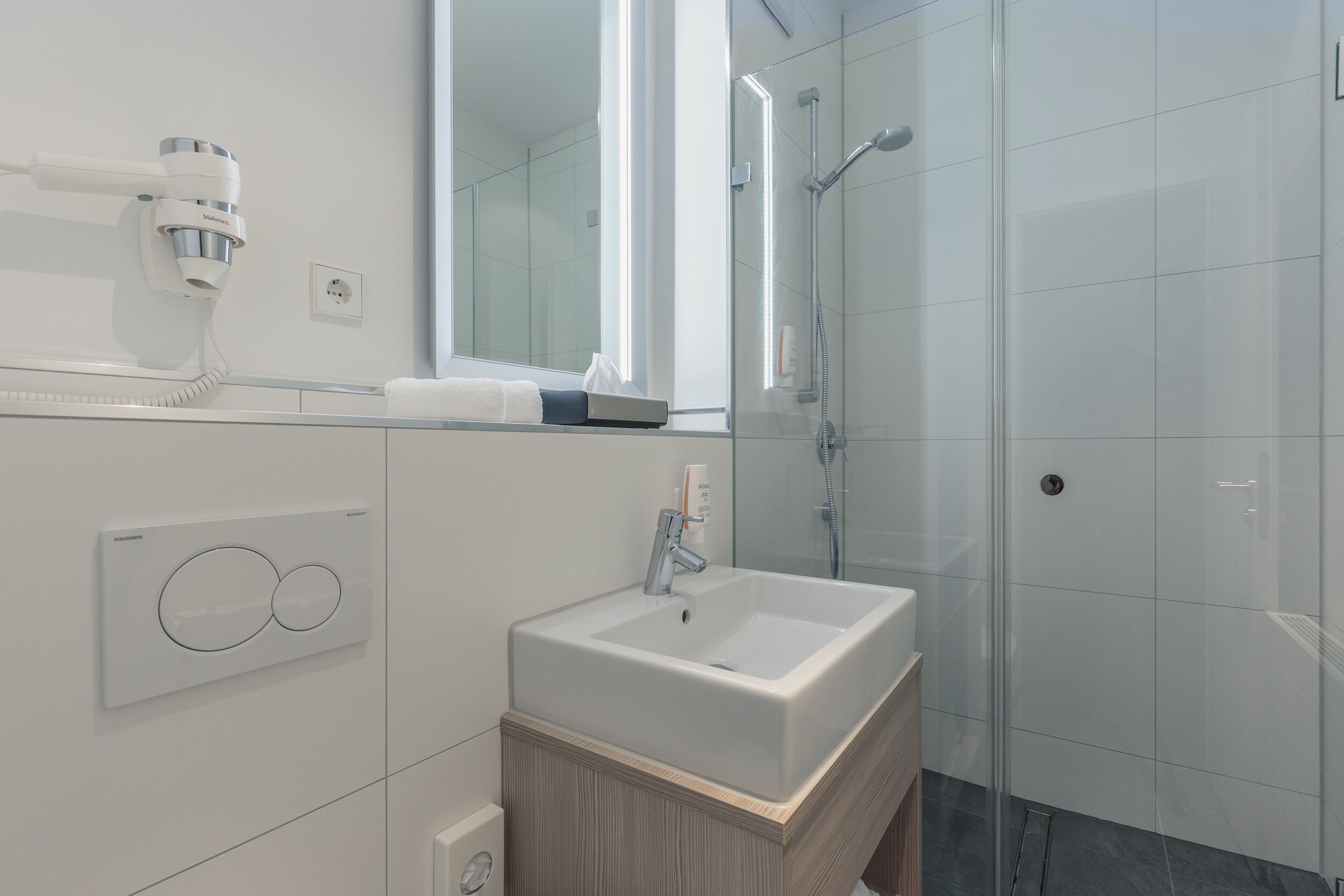 A modern bathroom with a white sink, a mirror, a handheld showerhead, and a toilet.