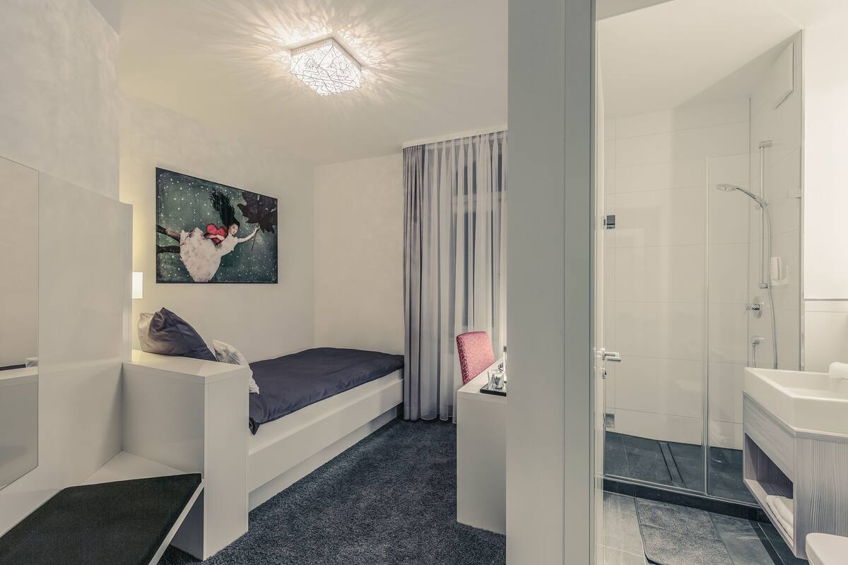 Un dormitorio moderno con cama, escritorio, un cuadro y zona de ducha.