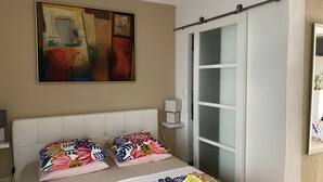 Un dormitorio con cama, mesita de noche, lámpara, un cuadro y una puerta corredera.