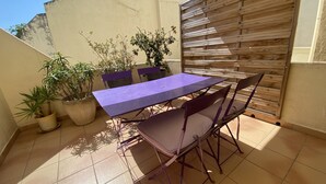 Un pequeño patio al aire libre con una mesa y sillas, rodeado de plantas en macetas y una valla de madera.
