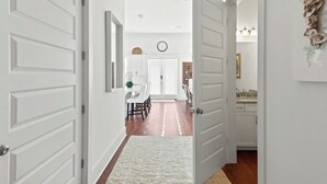 A hallway with white doors leading to a dining area and a kitchen. - LSV/Golf Cart, Private Pool, Fire Pit! Steps to Beach! Central Seagrove! Gulf Views!! (Santa Rosa Beach)