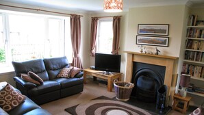 A living room with a sofa, television, fireplace, and bookshelf. - Popular Comfortable Well Equipped Cottage in Peaceful Ullapool Street w Parking (Ullapool)