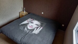 Un lit recouvert d’une couvre-lit grise ornée d’un portrait de célébrité et du mot « Glamour ».
