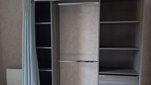 Un dressing avec de nombreuses étagères et un espace pour suspendre les vêtements, un rideau bleu clair et un luminaire blanc fixé au mur.
