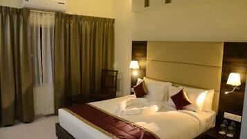 A hotel room with a large bed, two bedside lamps, a headboard, and an air conditioning unit.