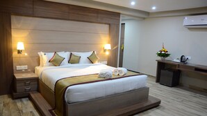 A hotel room with a large bed, bedside lamps, a desk with a coffee maker, and an air conditioner on the wall. - JAI MAATA GRANDEUR (Shimoga)