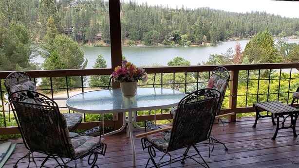 Un espacio de estar al aire libre cubierto con una mesa redonda y sillas, con vistas a un lago y una zona boscosa.