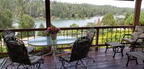 Un espace extérieur abrité, avec une table ronde et des chaises, offrant une vue sur un lac et une zone boisée.