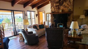Una sala de estar acogedora con chimenea de piedra, pisos de madera y un espacio de descanso cómodo con sofá y sillones.