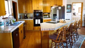 Una cocina con armarios de madera, una isla central con taburetes de bar, lavavajillas y refrigerador.