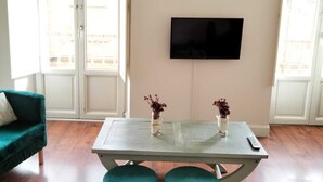 Una sala de estar moderna con piso de madera, un sofá verde, una mesa de centro de vidrio con dos jarrones y un televisor de pantalla plana montado en la pared.
