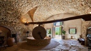 A stone-walled room with a large stone mill wheel, a wooden beam ceiling, and a rustic stone floor.