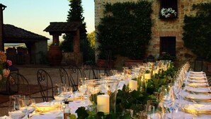 An outdoor dining area with tables set for a meal, surrounded by greenery and stone walls.