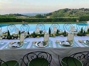 Une table à manger dressée pour un repas, avec une vue sur une piscine et des collines en arrière-plan.